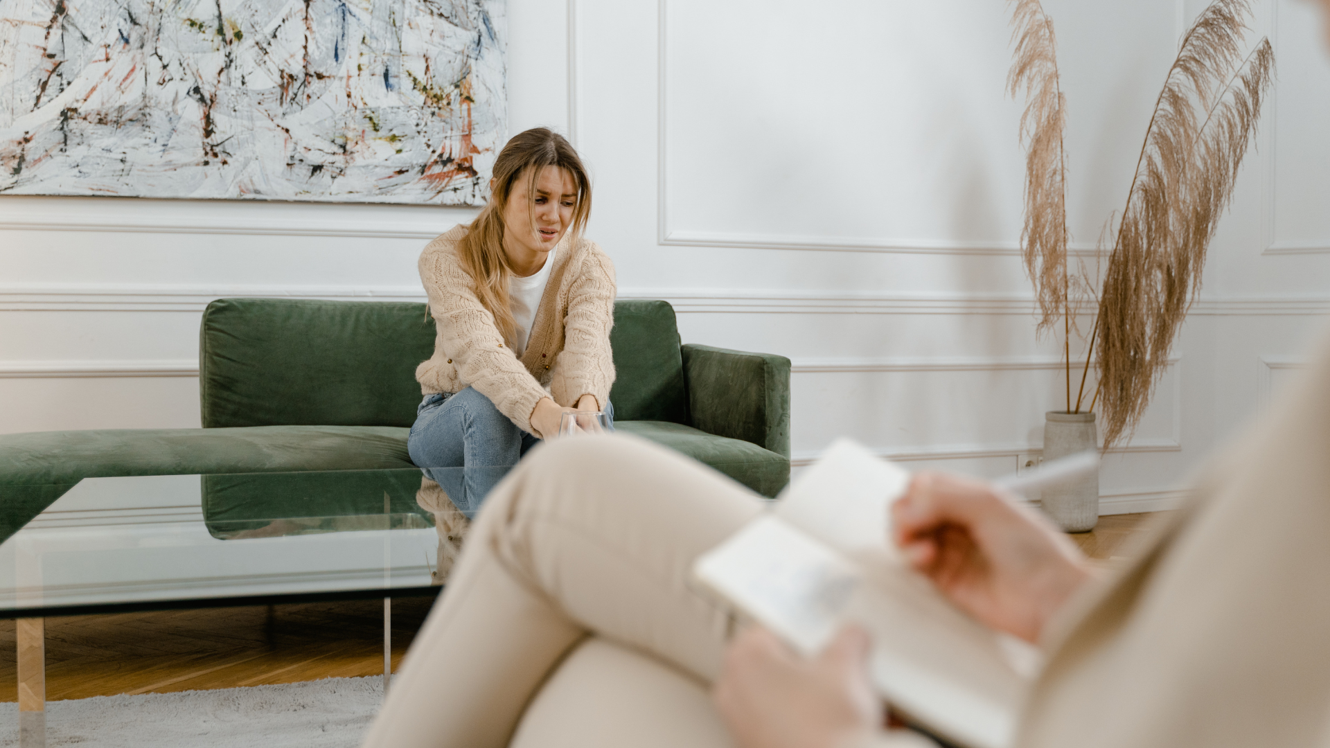A woman sitting on a green sofa in a therapy session, speaking with her therapist